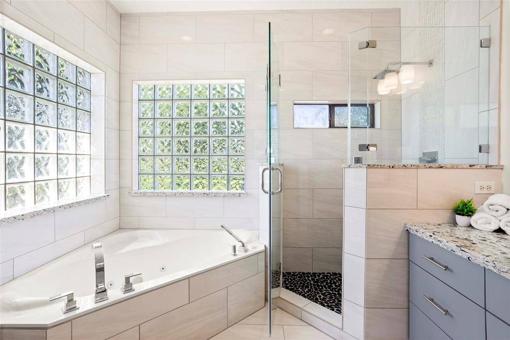 Experience luxury in the primary bathroom with a spacious walk-in shower, elegant corner bathtub, and sleek granite countertops. Large glass block windows flood the room with natural light while ensuring privacy.