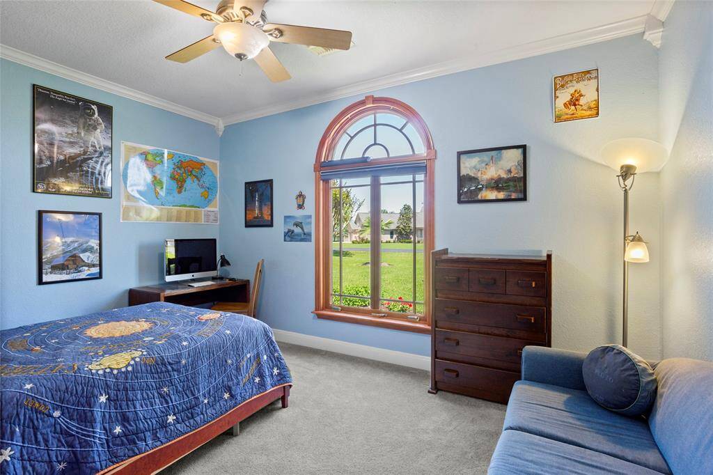 Downstairs bedroom #3 features a large arched window with a view of a lush green lawn and features a large walk-in closet with built-in shelving.