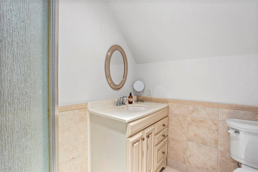 This upstairs bathroom features a vanity, a glass-enclosed shower, and tiled walls, offering a cozy and functional space.