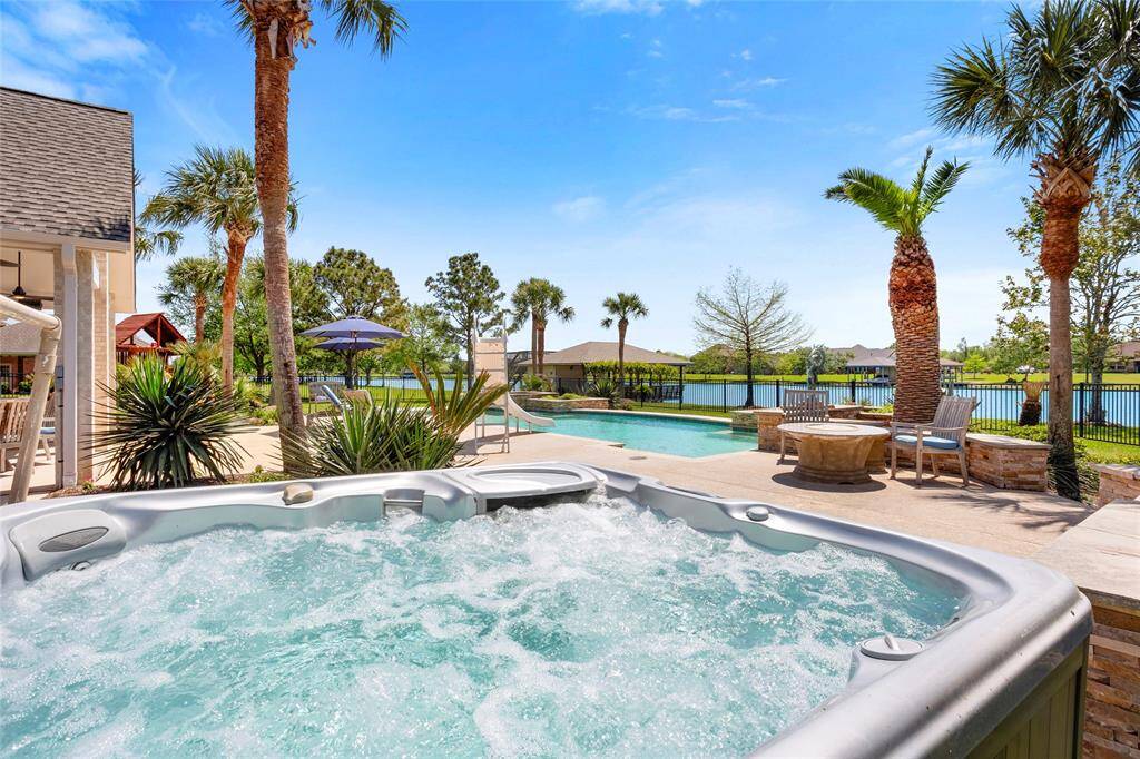 This backyard oasis features a luxurious hot tub, a sparkling pool, and a spacious patio with palm trees and lake views, perfect for relaxation and entertaining.