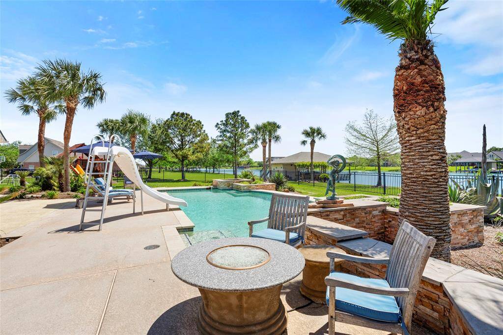 This stunning outdoor space boasts a pool with a slide, surrounded by palm trees and lush greenery. Enjoy a cozy seating area with a fire pit, perfect for relaxation and entertaining, all overlooking a serene lake.