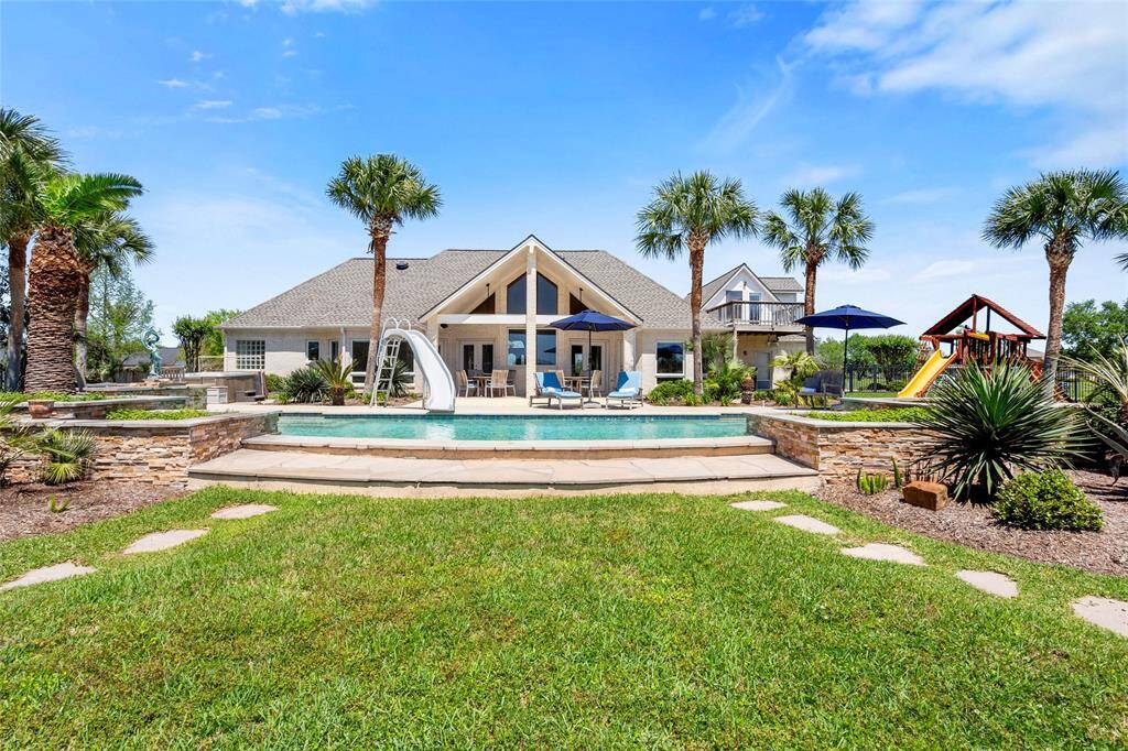 This 1-acre oasis featuring a spacious backyard with a pool, slide, and stylish stone planters. Enjoy a play area with a swing set and slide, surrounded by palm trees and lush greenery—perfect for family fun and relaxation.