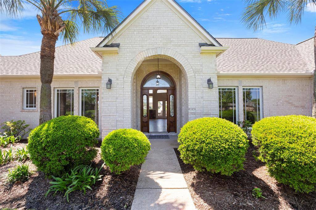 Charming custom home with a welcoming arched entrance, framed by lush greenery and palm trees.