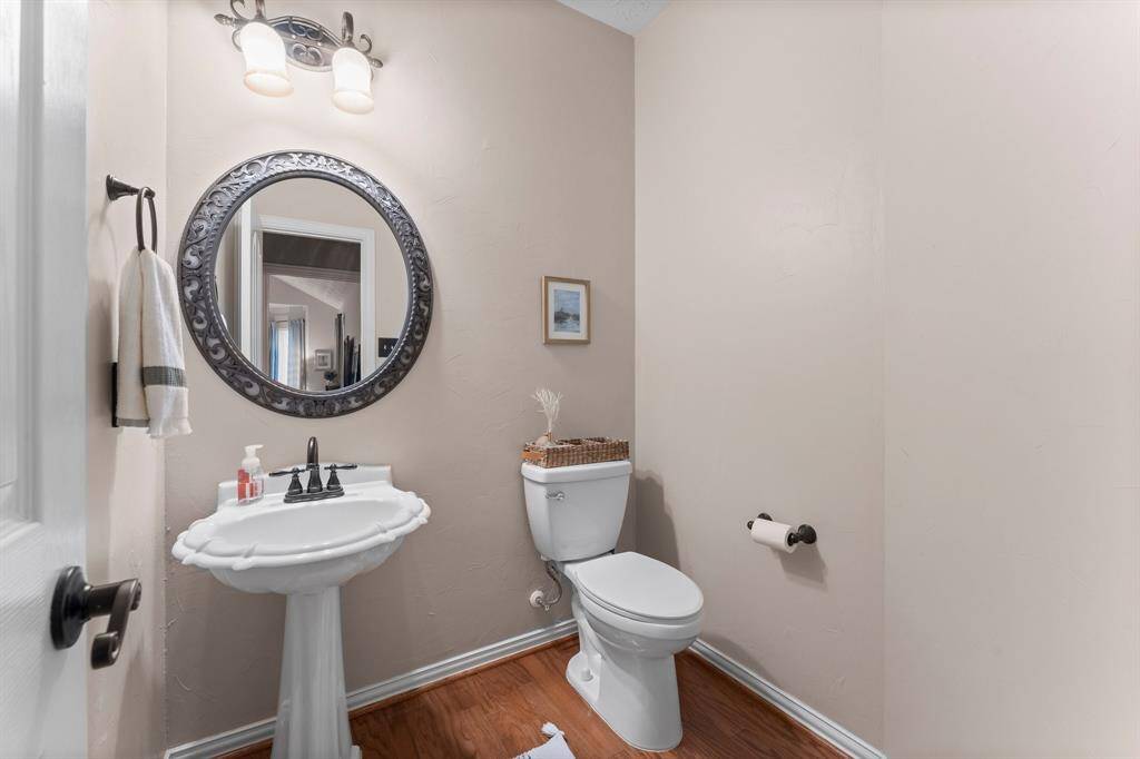 The formal guest bath features wood flooring, pedestal sink, toilet, and framed mirror.