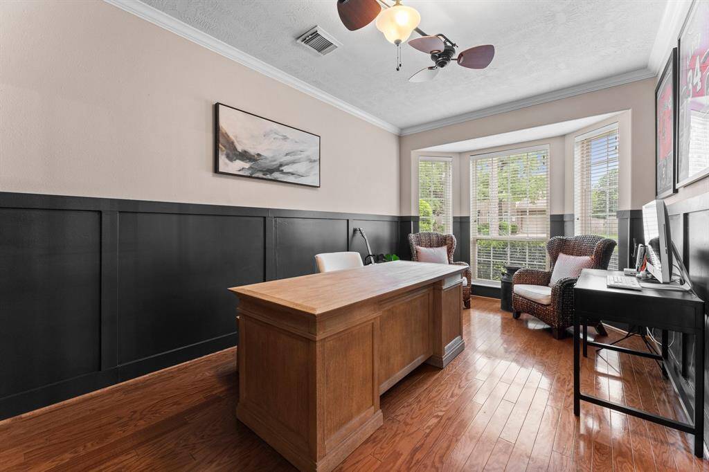 The executive office is a showstopper, featuring a half wall of custom woodwork added in 2022. A bay window floods the room with natural light. Additional features include wood flooring, crown molding, and lighted double ceiling fan.