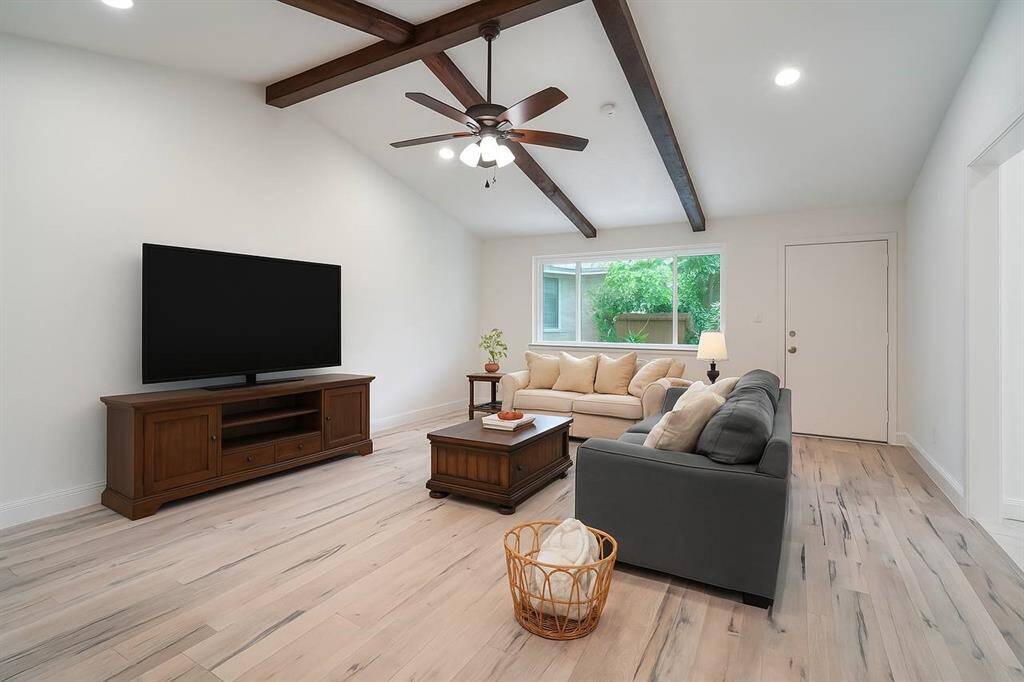 The open living area features a vaulted ceiling with exposed beams with ample natural lighting Virtually enhanced.