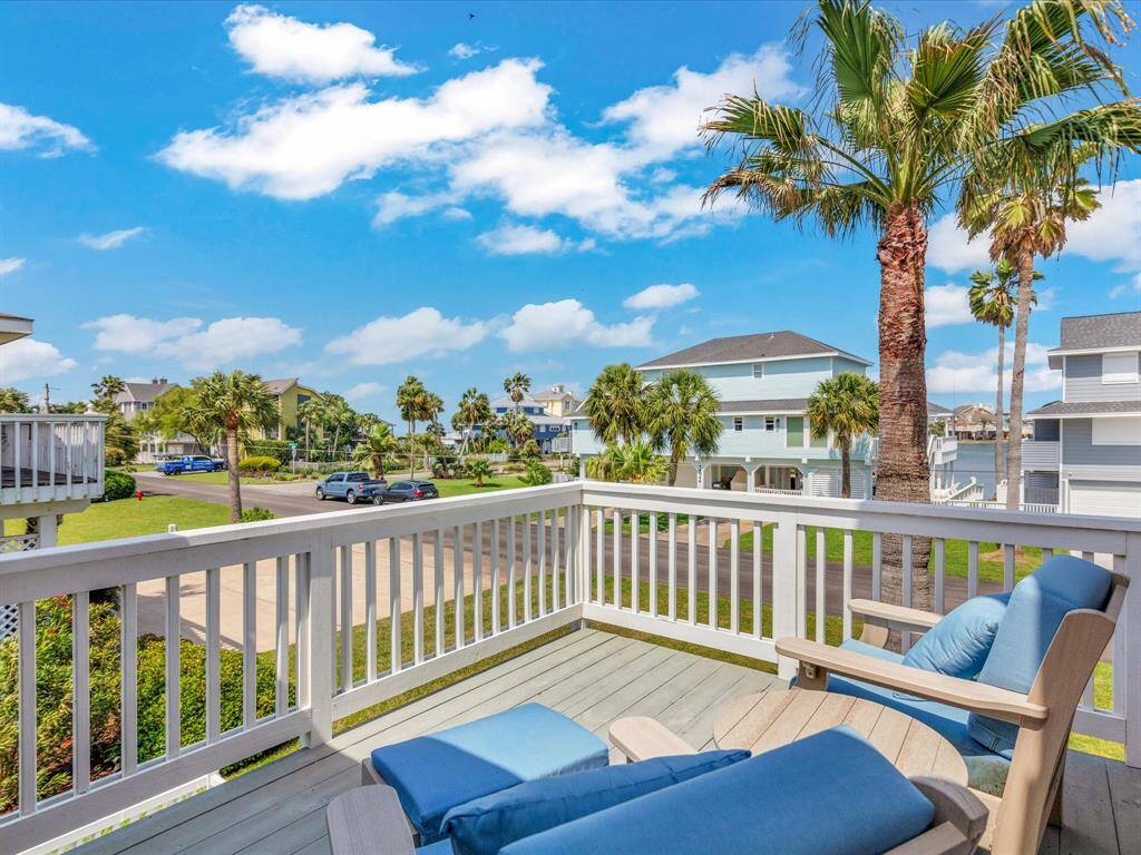 Inviting front balcony with comfortable seating, offering a view of a quiet neighborhood street lined with palm trees & West bay in the distance. Enjoy a morning cup of coffee as you take in the views.