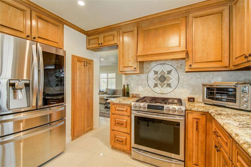 A close-up view of the gas stove and oven highlights a beautifully tiled backsplash, with a glimpse of the formal living room visible in the background.