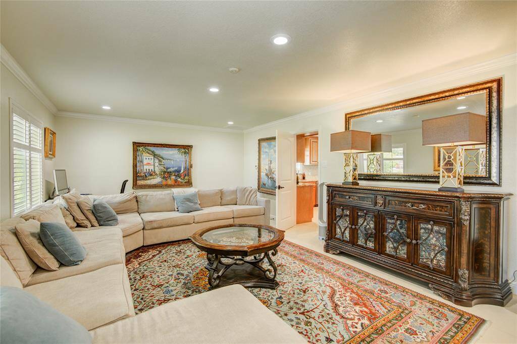 The expansive formal living room features crown molding, recessed lighting, and is bathed in natural light from large outdoor-facing windows.