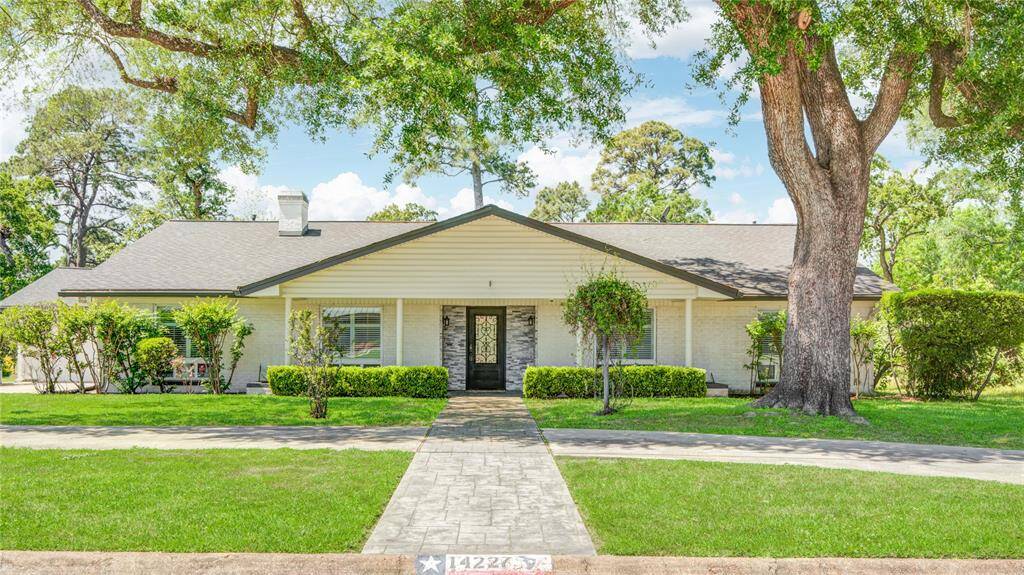 This white brick ranch-style home features a circular driveway, covered front porch, and surrounding mature trees and lush landscaping.