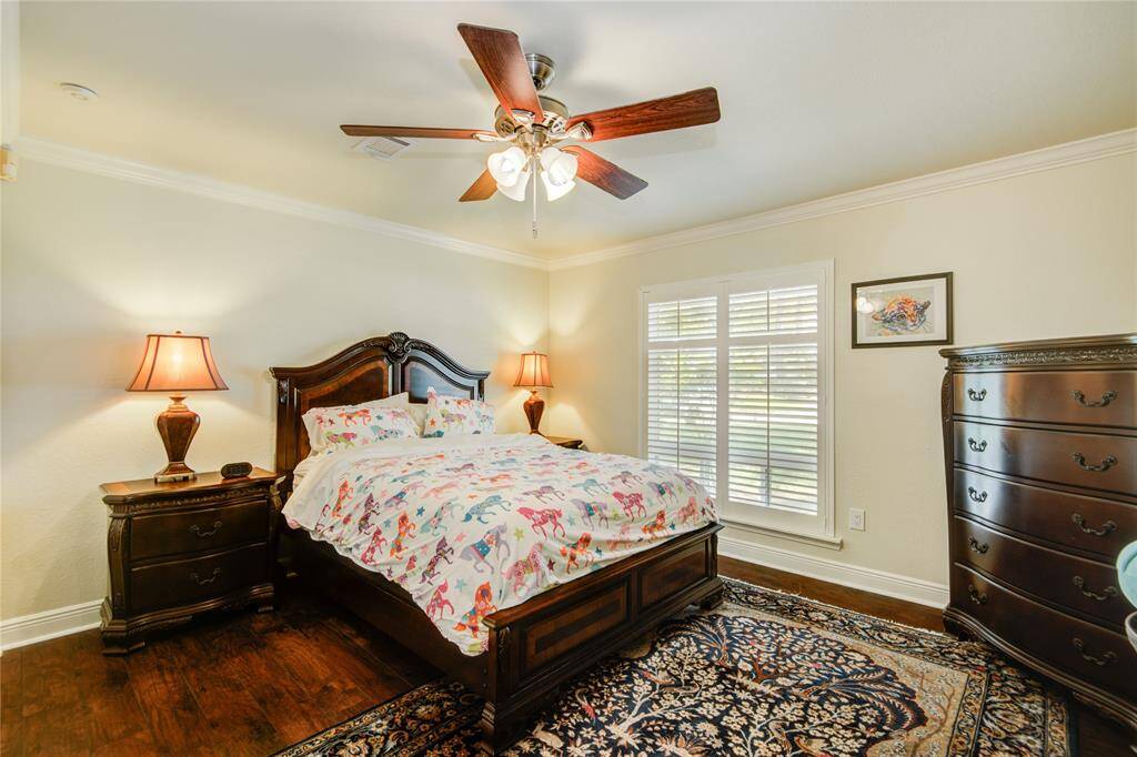 The second secondary bedroom, slightly larger than the first, mirrors the same neutral palette and crown molding, complemented by warm wood floors that add a cozy touch.