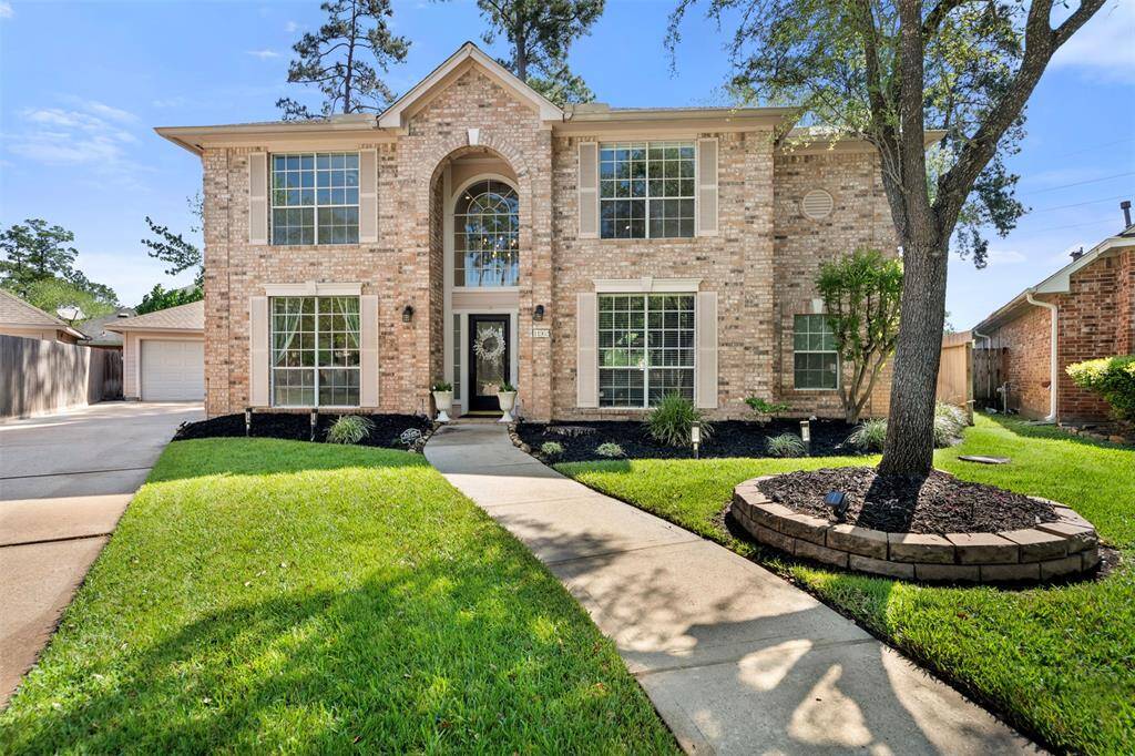 This photo showcases a charming two-story brick home with large windows, a well-maintained front yard, and a curved pathway leading to the entrance. The house has a classic design and is surrounded by mature trees, offering a welcoming and serene environment.