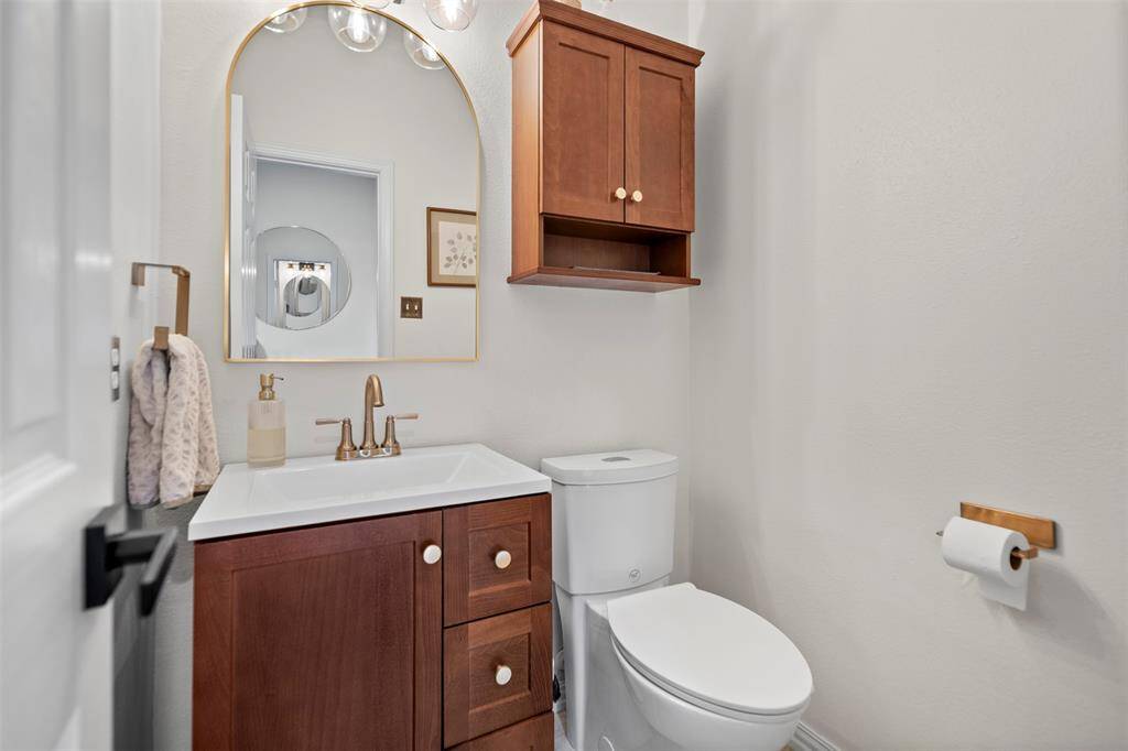 This modern bathroom features a sleek vanity with a wood cabinet, a stylish mirror, a compact toilet, and a wooden wall cabinet for extra storage. The neutral color palette and elegant fixtures create a clean, contemporary look.