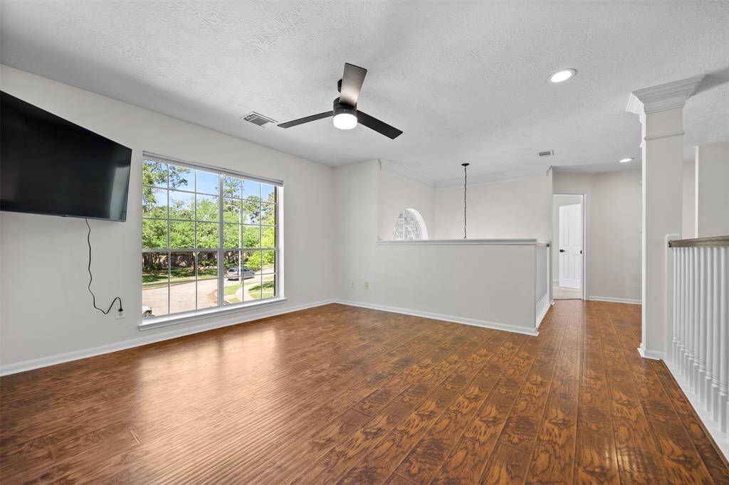 Bright and airy living space featuring large windows, beautiful hardwood floors, and a ceiling fan for added comfort. Modern lighting fixtures enhance the room’s contemporary feel, while a mounted TV adds a sleek touch. An open loft overlooks the living area, adding character and a spacious vibe.