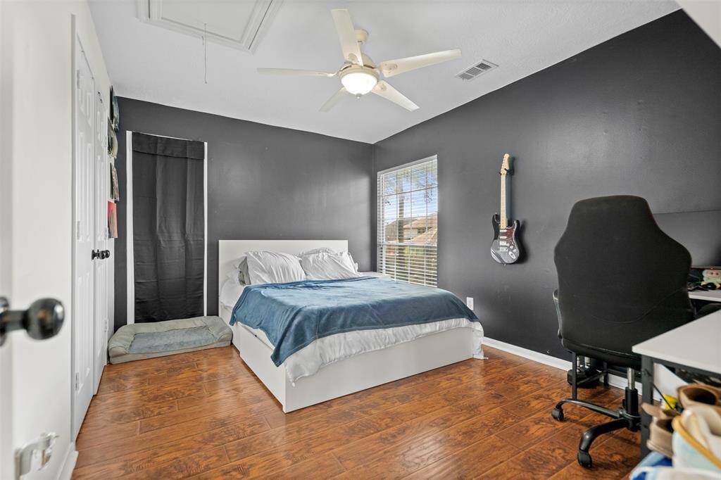 This bedroom features hardwood floors, a dark accent wall, and ample natural light from a large window.