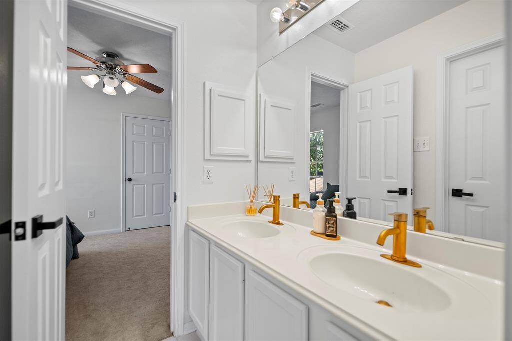 Modern bathroom with a dual-sink vanity featuring gold fixtures, white cabinetry, and a large mirror.