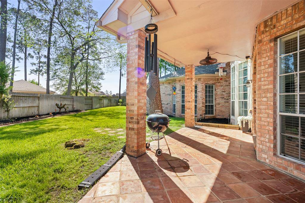 This inviting backyard features a spacious covered patio with terracotta tiles, ideal for outdoor entertaining. The lush green lawn is framed by tall trees and a wooden fence, providing privacy and a serene atmosphere.