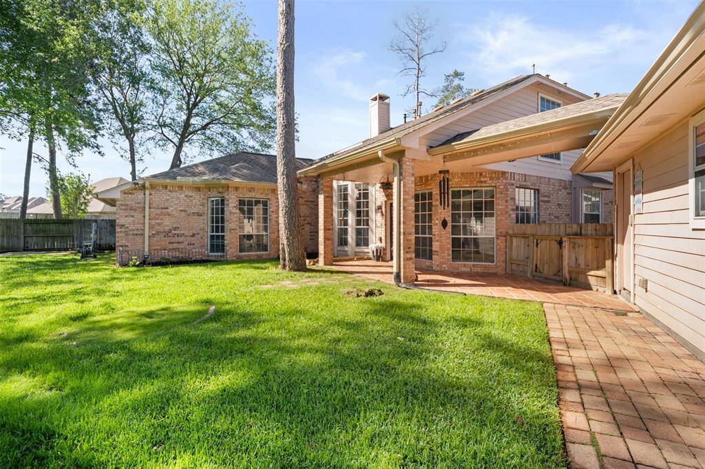 This photo highlights a generous backyard with vibrant green grass and mature trees providing natural shade. A covered patio extends from the brick home, creating an ideal space for relaxing or entertaining outdoors. The yard is beautifully maintained and features fruit trees, giving you your very own garden oasis at home.