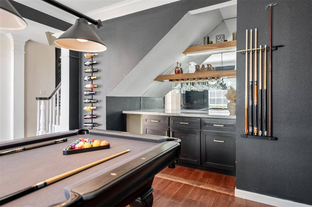This stylish room features a sleek pool table, a wall-mounted wine rack, and a mini bar area with hanging glassware and dark cabinetry, creating a perfect entertainment space.