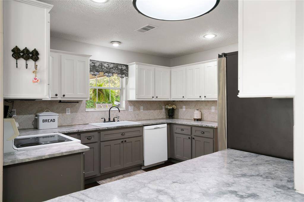 Crisp two-tone cabinetry, tiled backsplash, and solid surface countertops offer both style and storage. A window over the sink brings in natural light and a peaceful frontyard view.