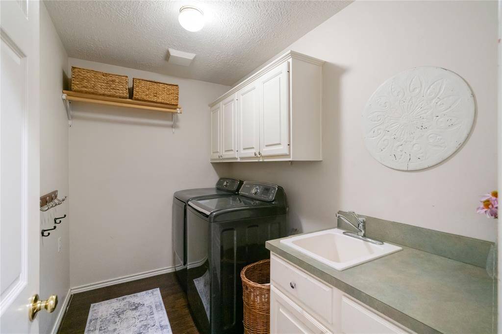 Well-equipped laundry room featuring upper cabinetry for storage, a utility sink with counter space, and a convenient hanging rack. Located near the main living areas for easy access.