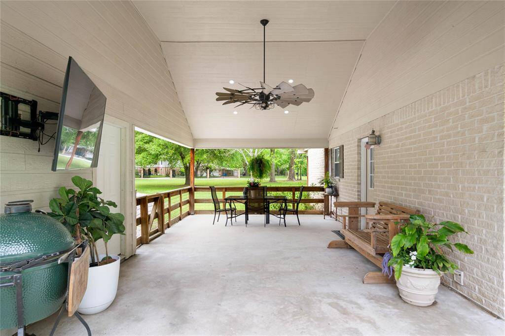 Covered patio situated between the main house and garage—ideal for outdoor dining, grilling, or watching the game. Features oversized ceiling fans, mounted TV, and room for both lounge and dining furniture.