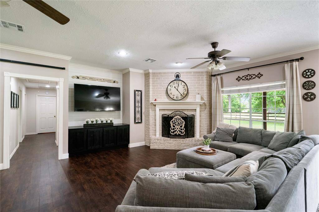 Open-concept living area with rich wood-style flooring, crown molding, and seamless flow into the dining and kitchen spaces.