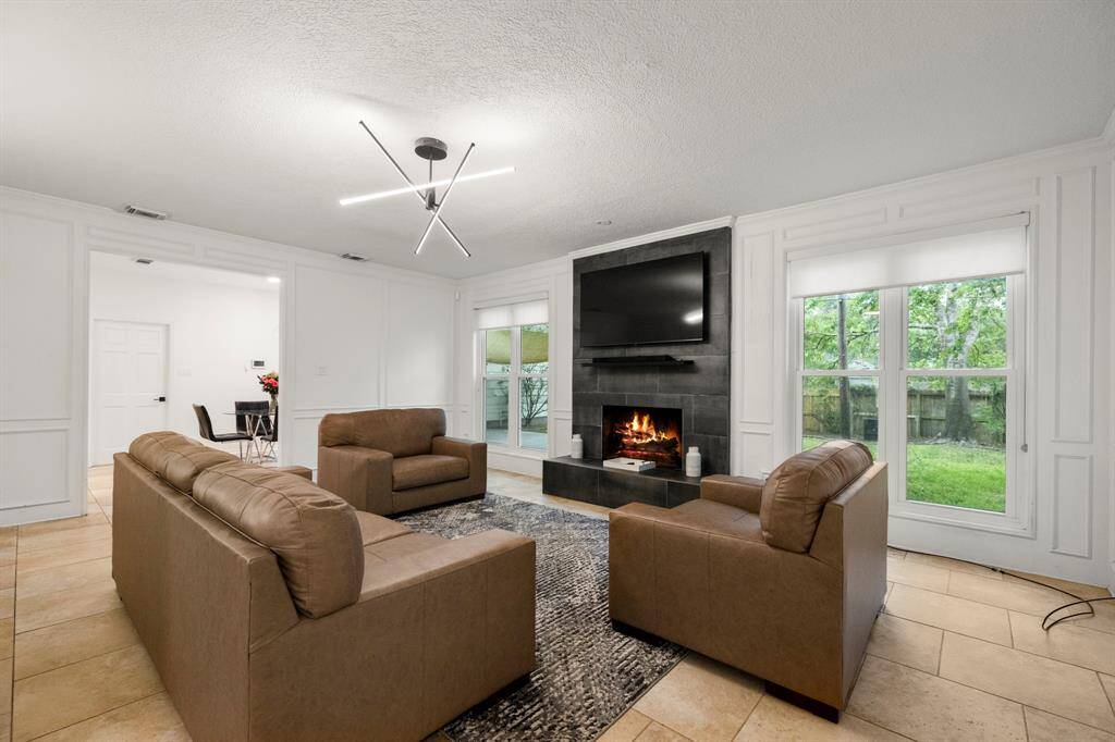 From this angle, the living room is bathed in natural light, highlighted by a modern light fixture that adds a touch of elegance. The open flow into the breakfast room is visible, creating a seamless connection between the spaces and enhancing the home’s open, inviting atmosphere.