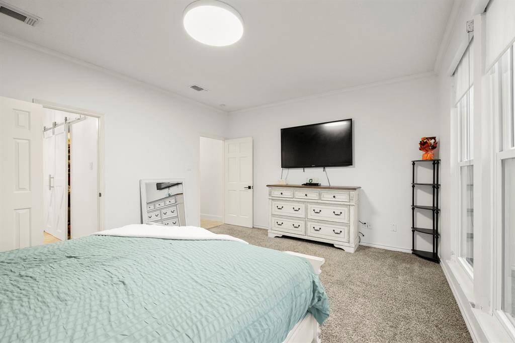 From this angle, we get a glimpse into the primary bath, with a sliding barn door leading to the walk-in closet. The doorway by the dresser provides easy access back to the living room, maintaining a seamless flow throughout the home.