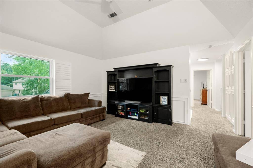The upstairs living area/game room features chair railing and vaulted ceilings, creating an open, airy feel. A large window allows natural light to flood the space. From here, you can also see the built-in cabinets in the hallway, adding both functionality and style to the area.