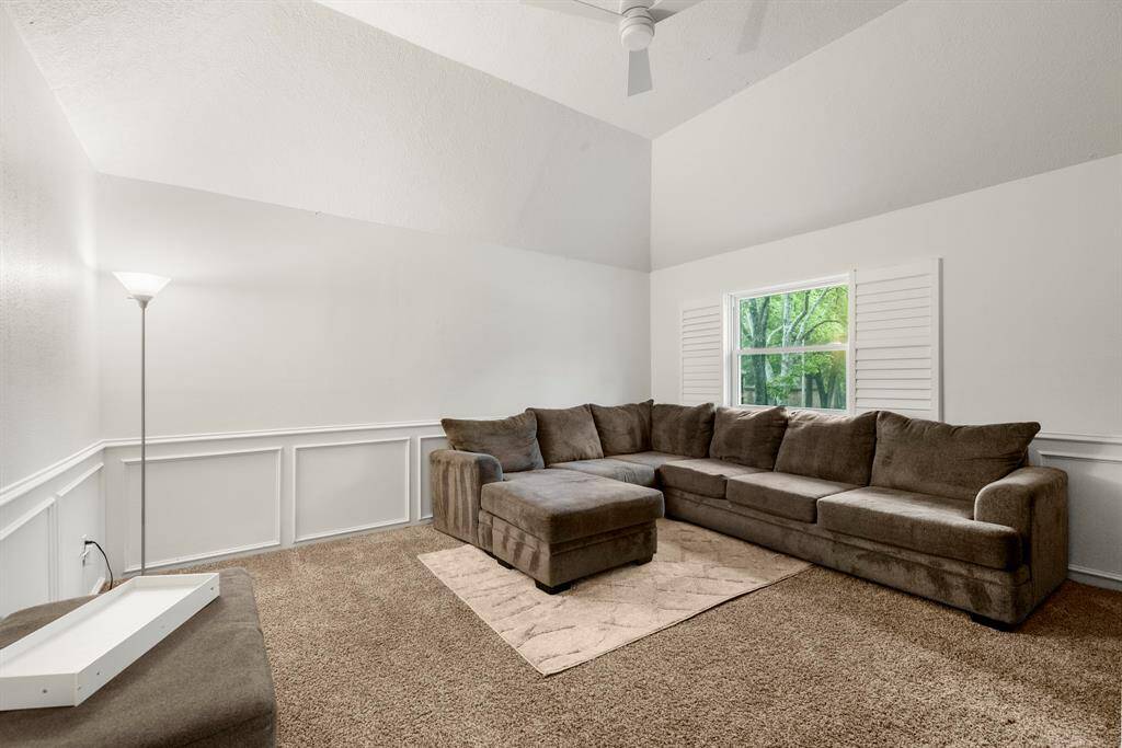Another view of the upstairs living area/game room showcases the open, airy atmosphere, with ample space for entertainment or relaxation. The vaulted ceilings add to the room's expansive feel, while the large window continues to bring in natural light, brightening the space.