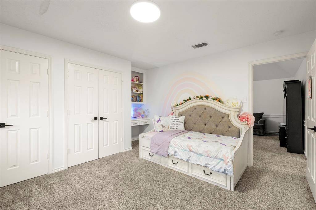 This upstairs bedroom, just off the game room, features two closets for ample storage space. A built-in desk area adds functionality, making it the perfect spot for studying or working from home, while the room remains bright and inviting.