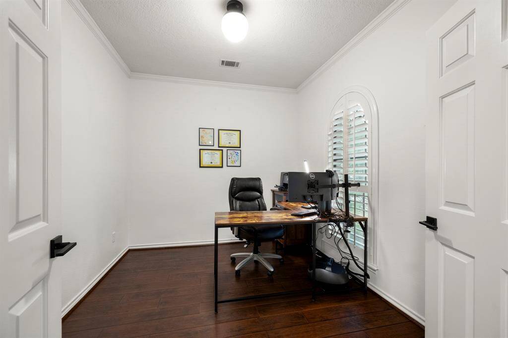 A closer look inside the home office, featuring plantation shutters on the window that overlooks the front yard. Wood floors and crown molding add a touch of elegance, creating a productive and stylish space.