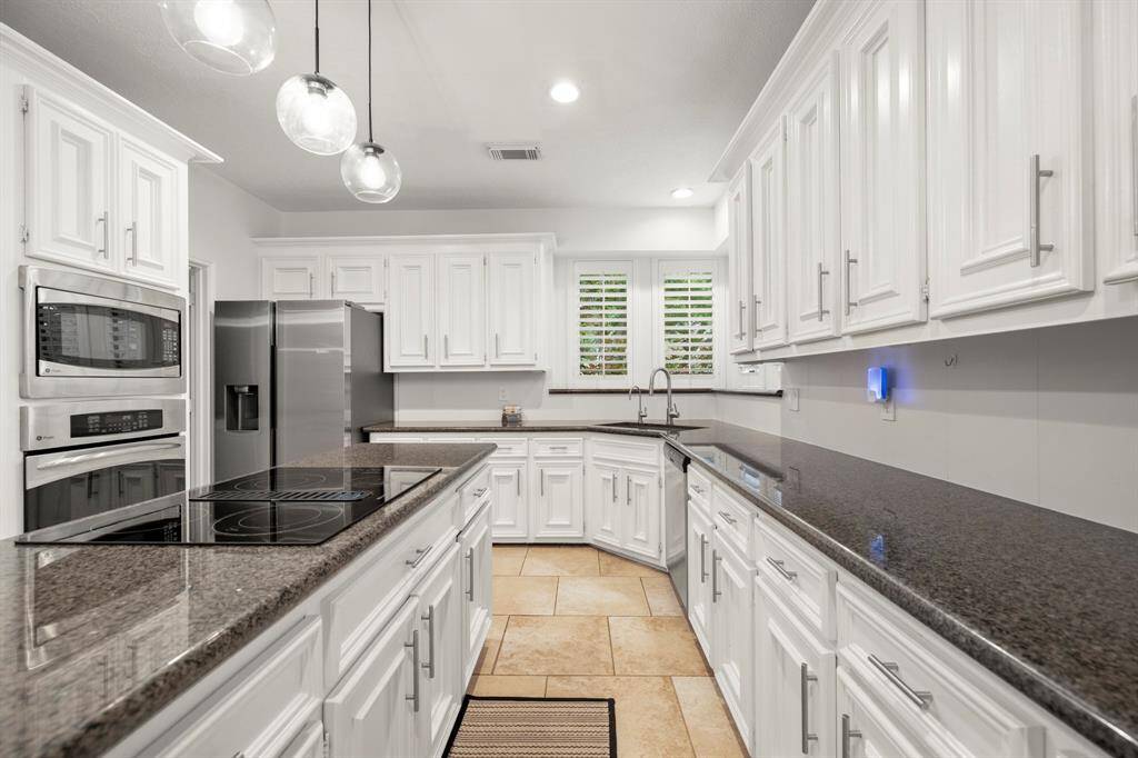 A closer view of the kitchen showcases the intricate detailing in the cabinetry trim, adding an elegant touch. The glass cooktop with a down draft vent is complemented by a built-in stainless oven and microwave. A closer look at the sink reveals a pull-down faucet and a convenient water faucet, making the space as functional as it is beautiful.