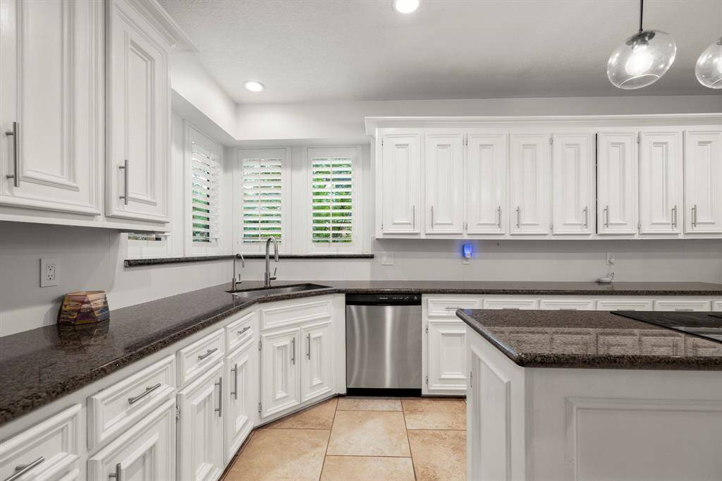 Another view of the kitchen highlights the corner sink, with the dishwasher conveniently located next to it. The windows above the sink are framed by plantation shutters on both sides, offering a bright view. A granite window ledge adds a stylish and functional touch to the space.