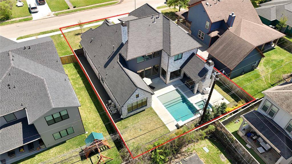 This aerial shot showcases a spacious, modern home with a gray exterior, featuring a private backyard pool. The property is well-defined with a red boundary line and sits in a suburban neighborhood with nearby homes.