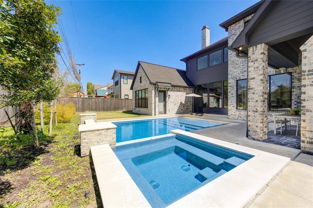 This photo showcases a modern home with a spacious backyard featuring a sleek pool and hot tub. The exterior is made of stylish stonework, and there's a covered patio area, perfect for outdoor relaxation and entertaining.