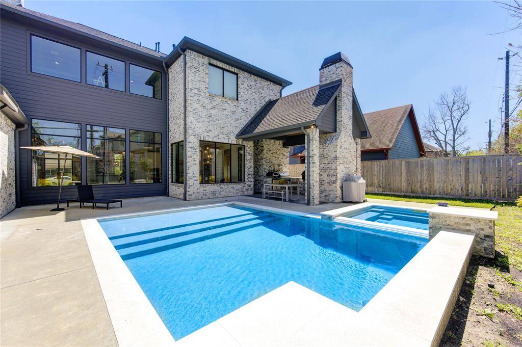 This photo showcases a modern home with a sleek exterior featuring a mix of brick and siding. It includes a spacious backyard with a pristine swimming pool, a covered patio area perfect for outdoor dining, and a privacy fence, creating a serene and inviting outdoor space.