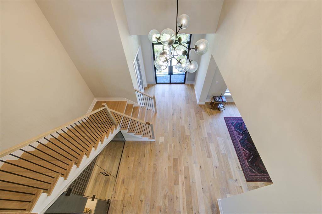 This photo showcases a spacious, bright entryway with a modern chandelier, light hardwood floors, and a stylish staircase. The area opens to a large glass door, offering an elegant and welcoming atmosphere.