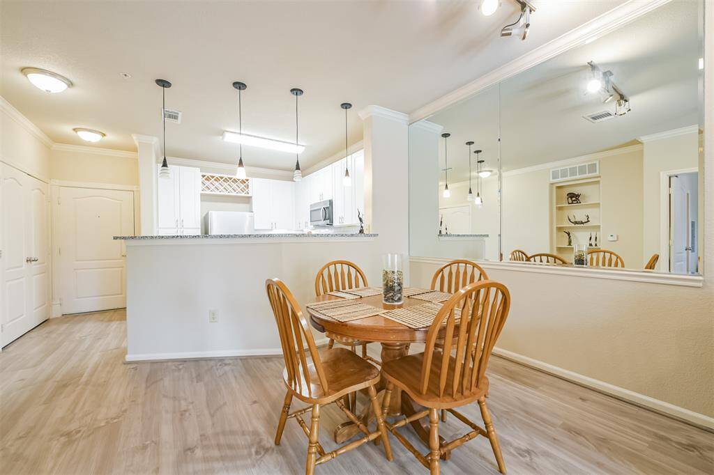 Bright and inviting living-dining area featuring hardwood floors, a cozy dining set, and a comfortable seating area. The room has ceiling fans, ample natural light from large windows, and elegant track lighting.