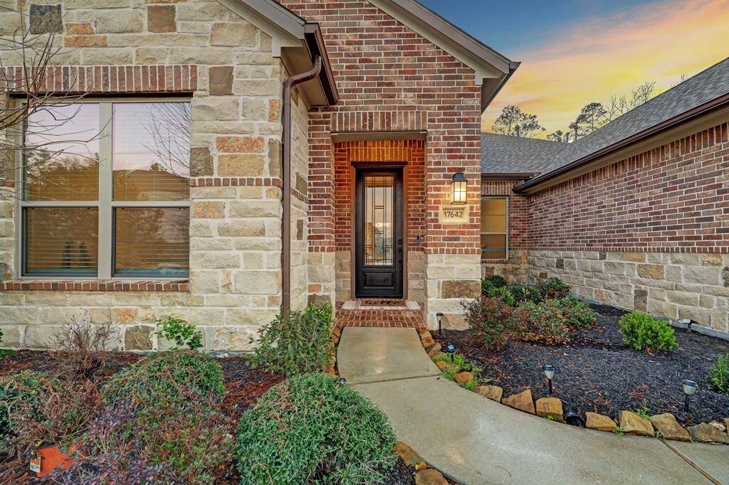 The entryway blends material richness with thoughtful proportion, featuring a striking combination of red brick and multi-tone stone that emphasizes texture and visual depth. A gently curved walkway guides you toward a recessed front door, framed by a modest overhang that offers both shelter and architectural definition. This composition creates a welcoming transition from public to private space while grounding the home's facade in classic, enduring design.