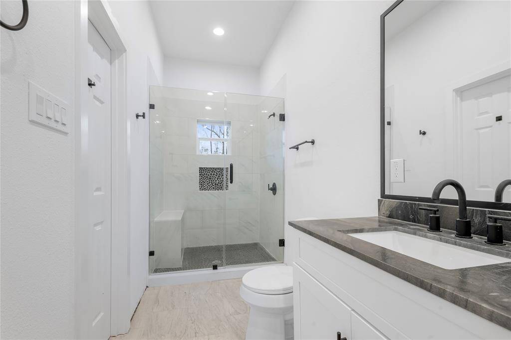 Primary bathroom features a spacious, modern design with a glass-enclosed shower, a sleek black countertop, and contemporary fixtures.