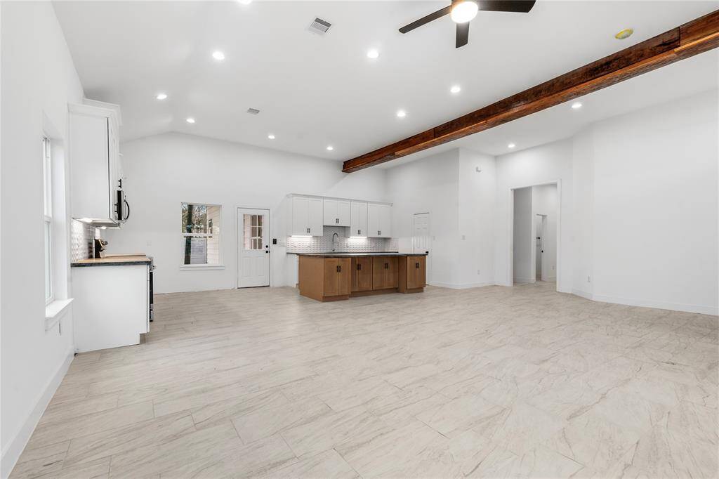Open-concept living area features a modern kitchen with a large island, high ceilings with recessed lighting, and a rustic wooden beam accent.