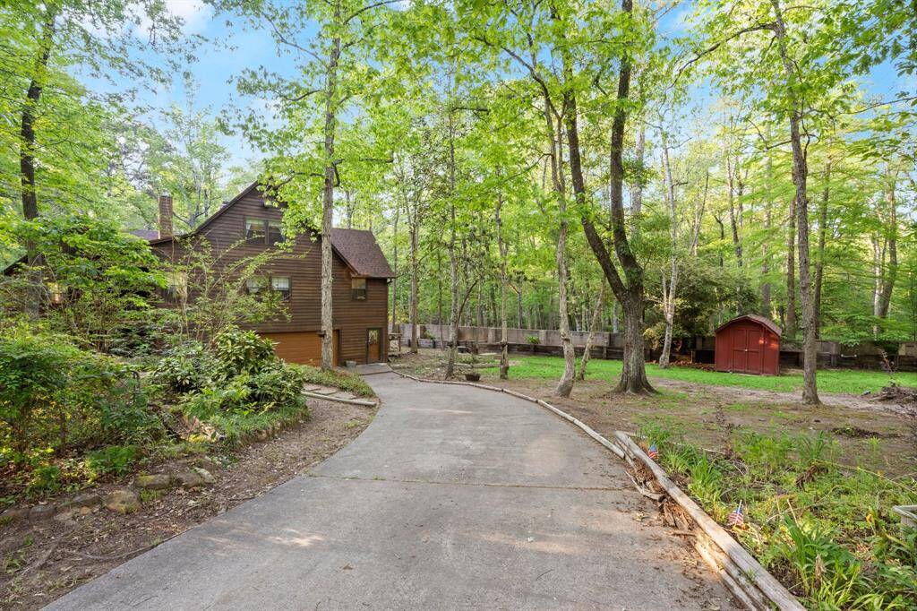 Welcome to your charming wood-sided home in a beautiful wooded setting. A curved driveway leads to the house, surrounded by mature trees and greenery, offering a serene, private atmosphere.