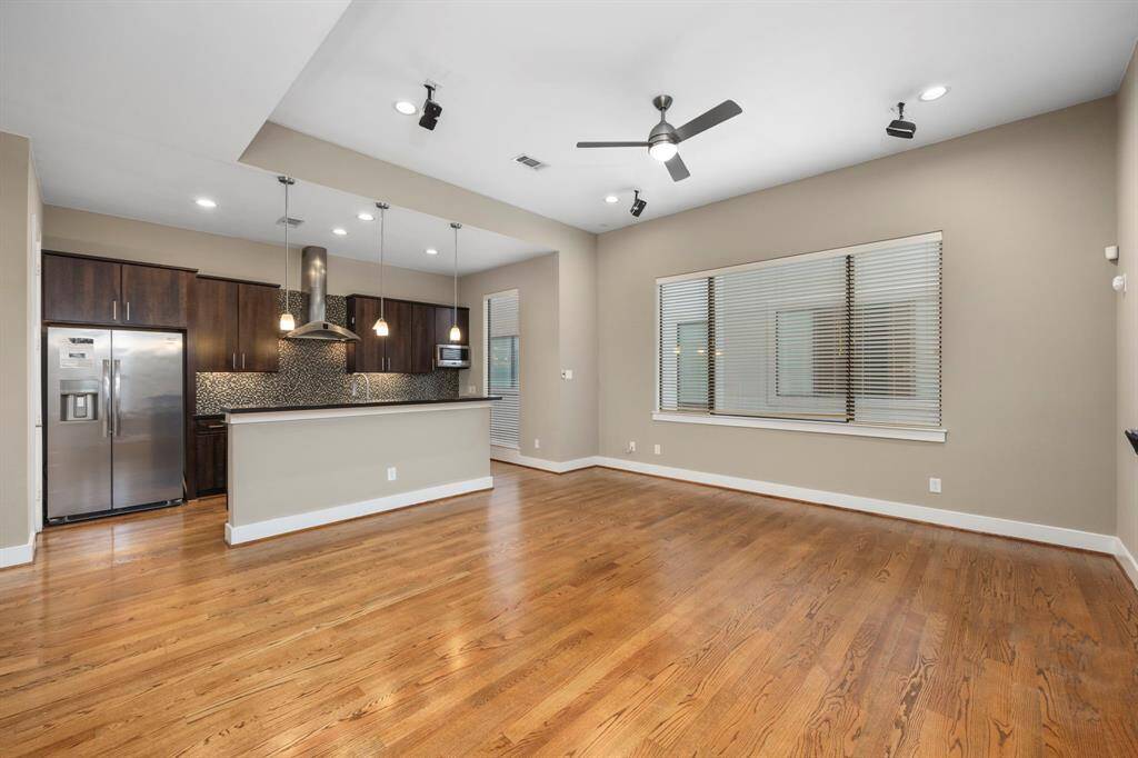 Living room features wood flooring, a ceiling fan, high ceilings, and large windows.