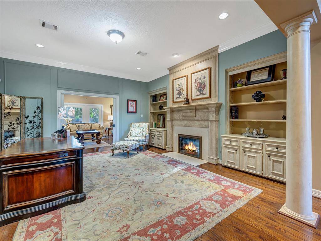 This elegant office or dining room features a cozy fireplace, built-in shelving, and classic wood flooring. The space is accented by a decorative pillar, an ornate area rug, and stylish furnishings, creating a warm and inviting atmosphere.