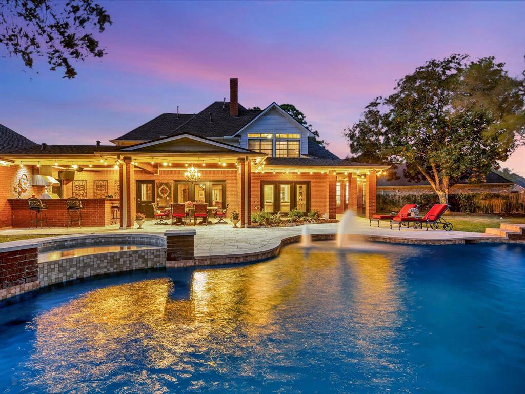 This stunning home features a spacious backyard with a beautifully lit pool and patio area, perfect for entertaining. The outdoor kitchen and dining space offer comfort and style, set against a picturesque sunset backdrop.