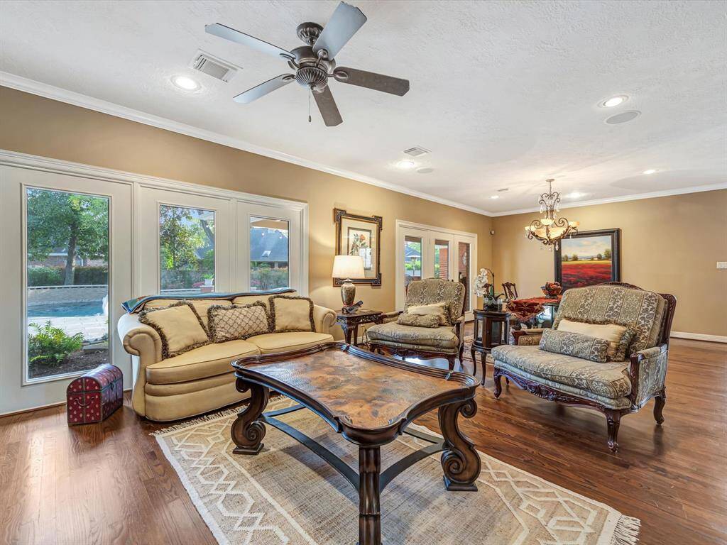 This spacious living room features elegant hardwood floors, large windows offering plenty of natural light, and a cozy seating area with classic furniture. It includes a view of the outdoor pool area, creating a perfect blend of indoor comfort and outdoor charm.