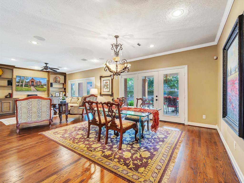 This spacious, elegant living area features hardwood floors and French doors leading to the patio. It combines a cozy sitting area with a dining space, highlighted by classic furniture and built-in shelving.