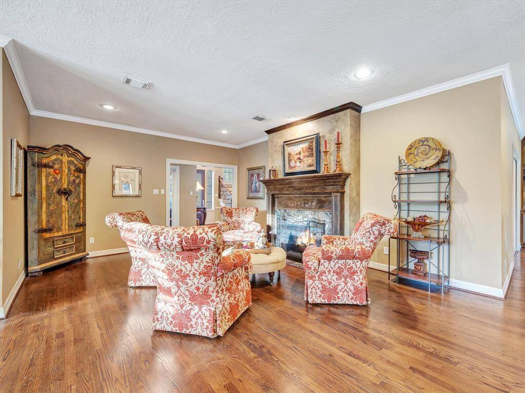 This living room features warm hardwood floors, a cozy fireplace, and elegant, patterned armchairs. The space is well-lit with recessed lighting and includes tasteful decor with a sophisticated ambiance.